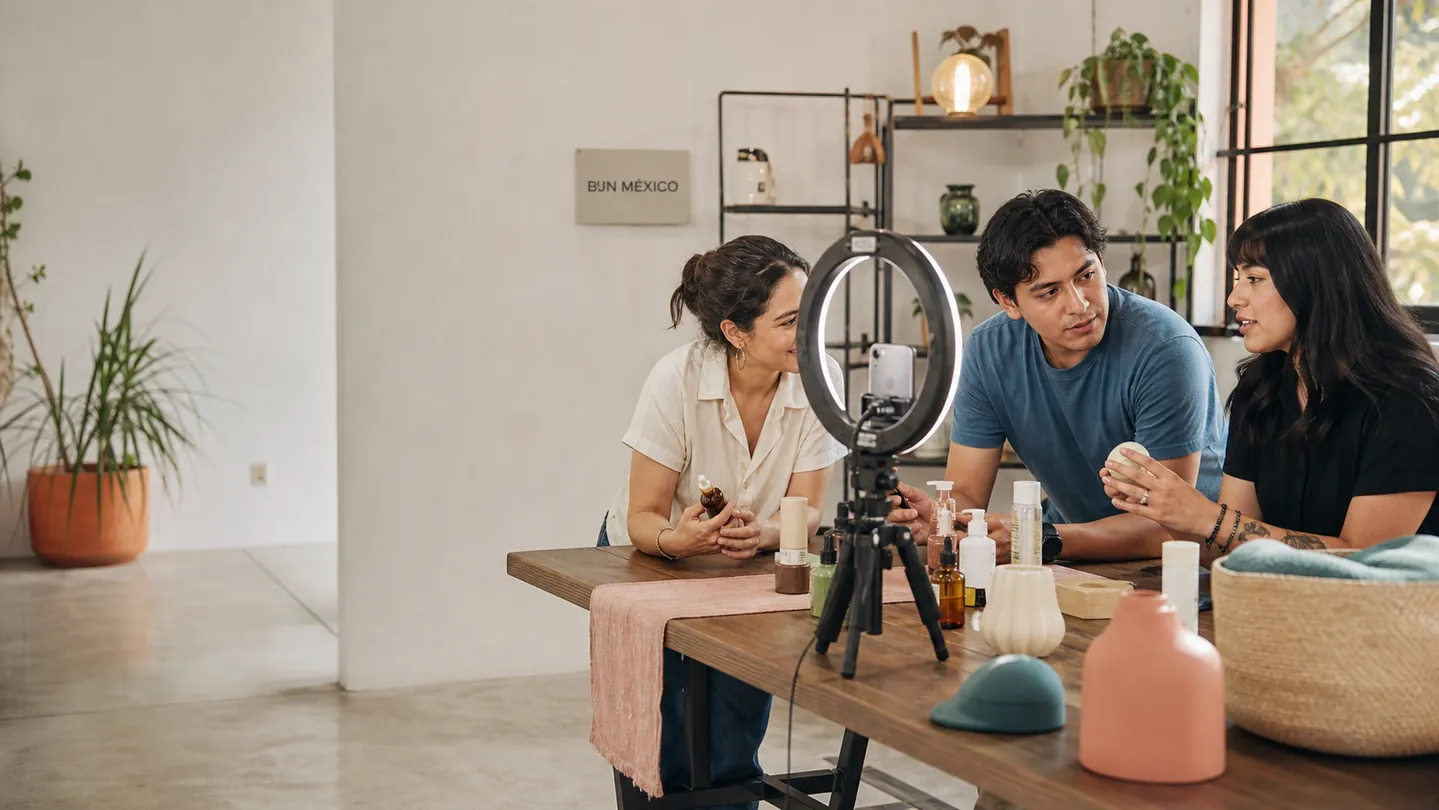Tres creadores revisan productos y preparan una transmisión con celular y aro de luz en un estudio BJN México